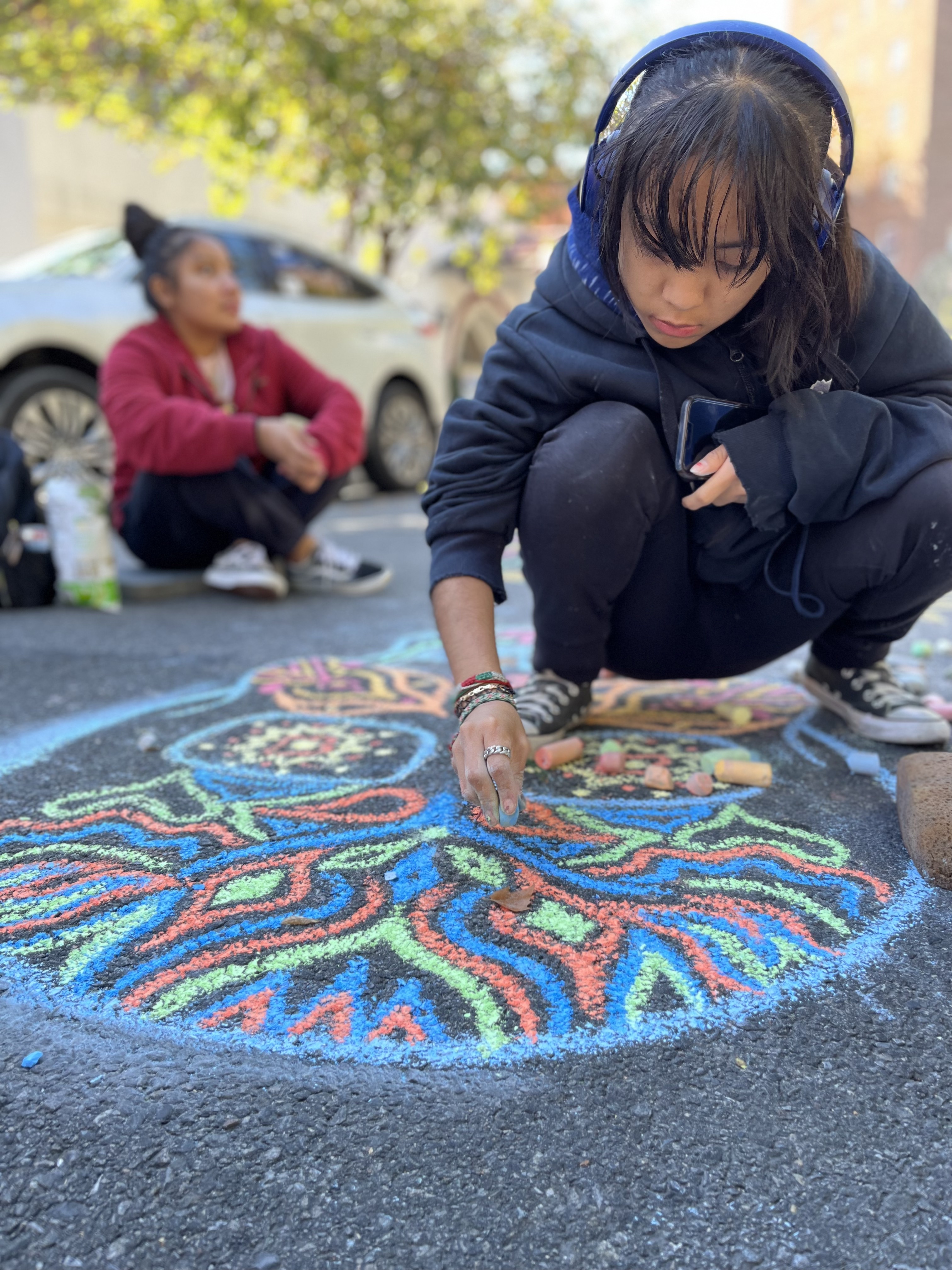 Student creating colorful chalk art designs on asphalt