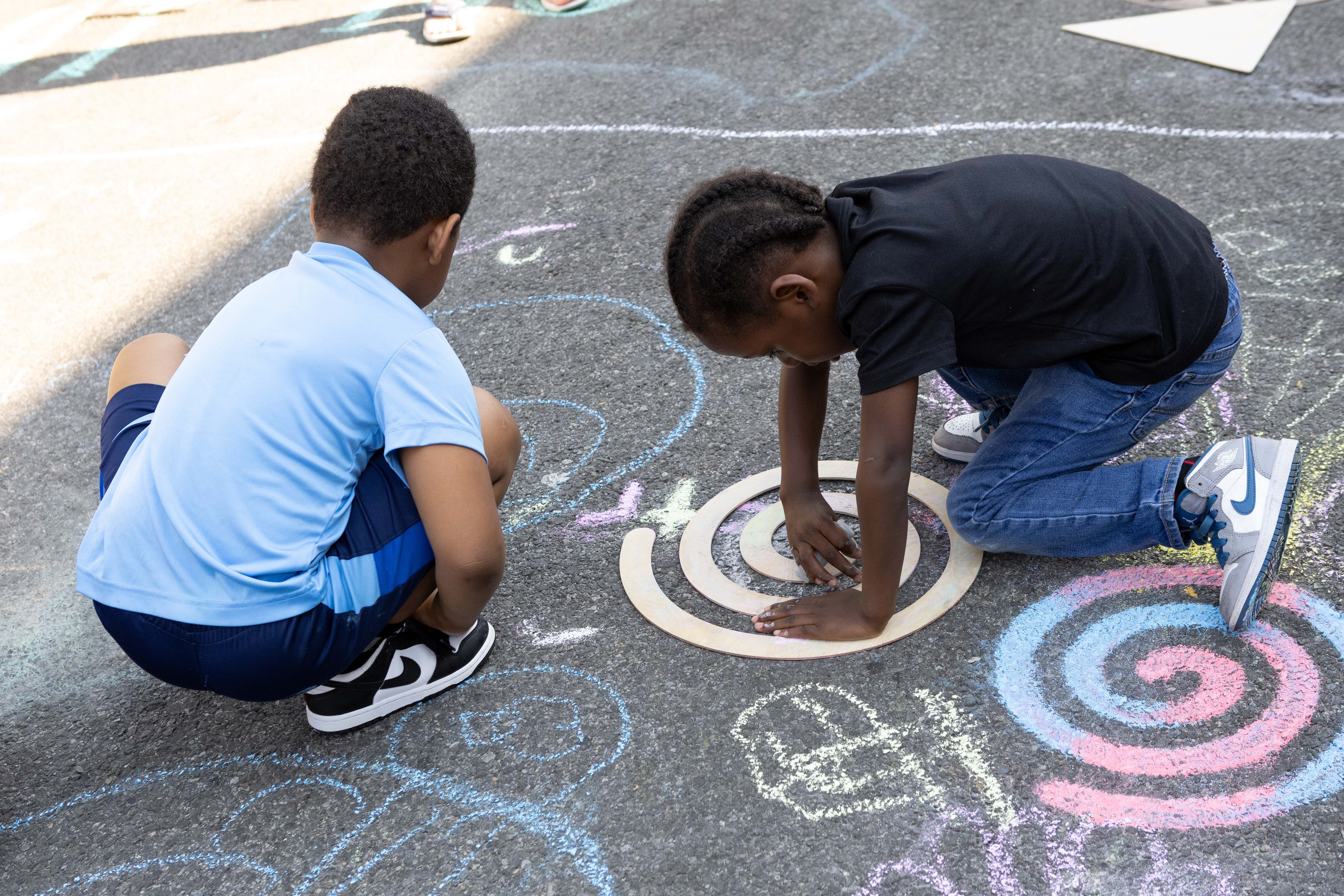 Children using circular templates to create chalk art designs